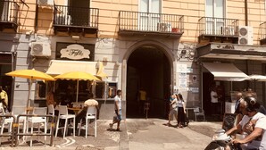 Une scène de rue avec des tables à l’extérieur, un café et un immeuble doté de balcons et d’enseignes.