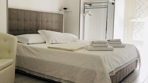 Un lit bien fait, avec un couvre-lit blanc et des oreillers, une table de chevet avec une lampe et une chaise.