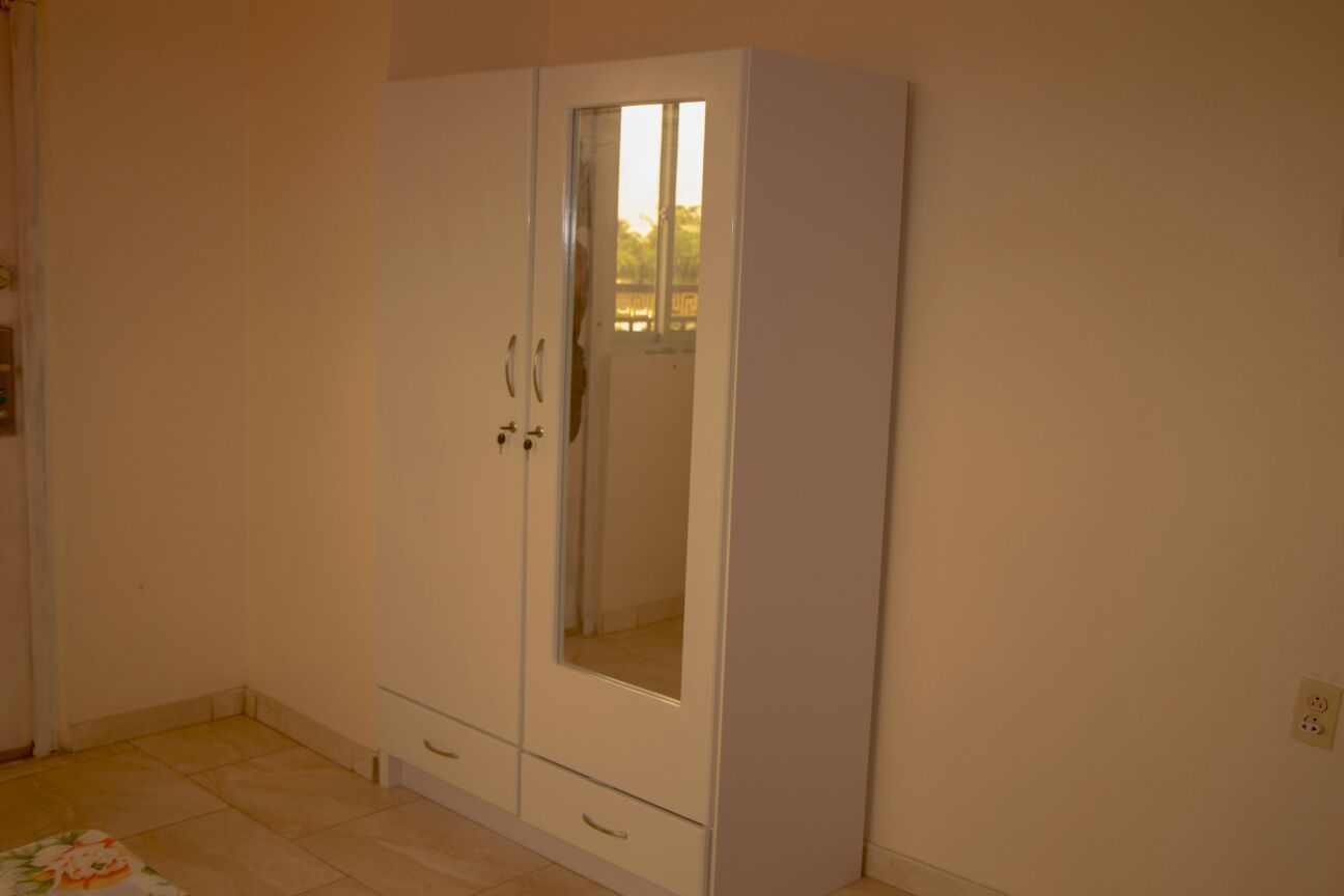 Ein Zimmer mit einem weißen Kleiderschrank, einem kleinen Fenster und einem Fliesenboden.