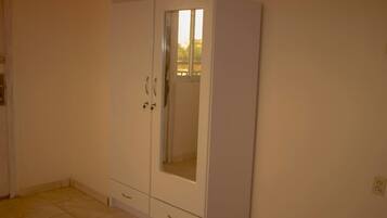 Ein Zimmer mit einem weißen Kleiderschrank, einem kleinen Fenster und einem Fliesenboden.
