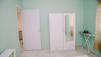 A bedroom with a bed, a wardrobe, a mirror, and a small table with an ironing board.