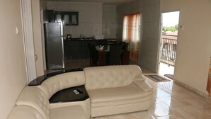 Uma sala de estar com um sofá seccional bege, uma mesa de centro preta e uma cozinha ao fundo.