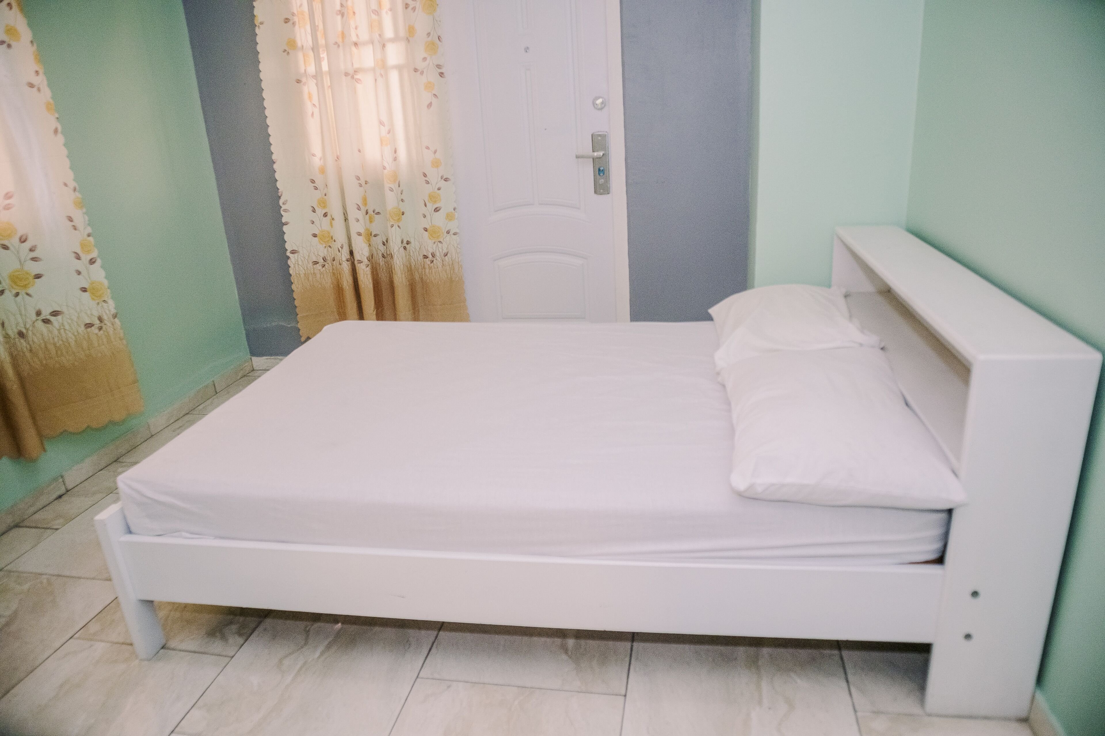 A single bed with white bedding in a room with light green walls and a white door.