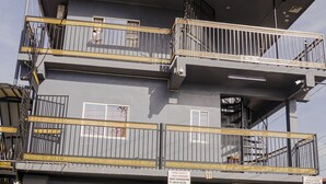 Um edifício de vários andares com varandas, uma loja fechada no térreo e uma escadaria visível.