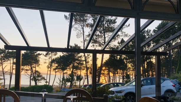 Mesa lista para cenar con vista a la puesta de sol sobre el agua y los árboles.
