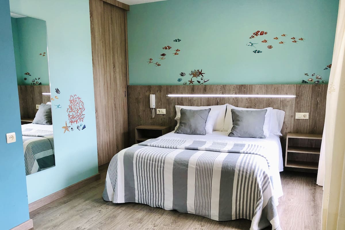Un dormitorio con cama, mesitas de noche, un espejo y una pared decorada con calcomanías de peces.