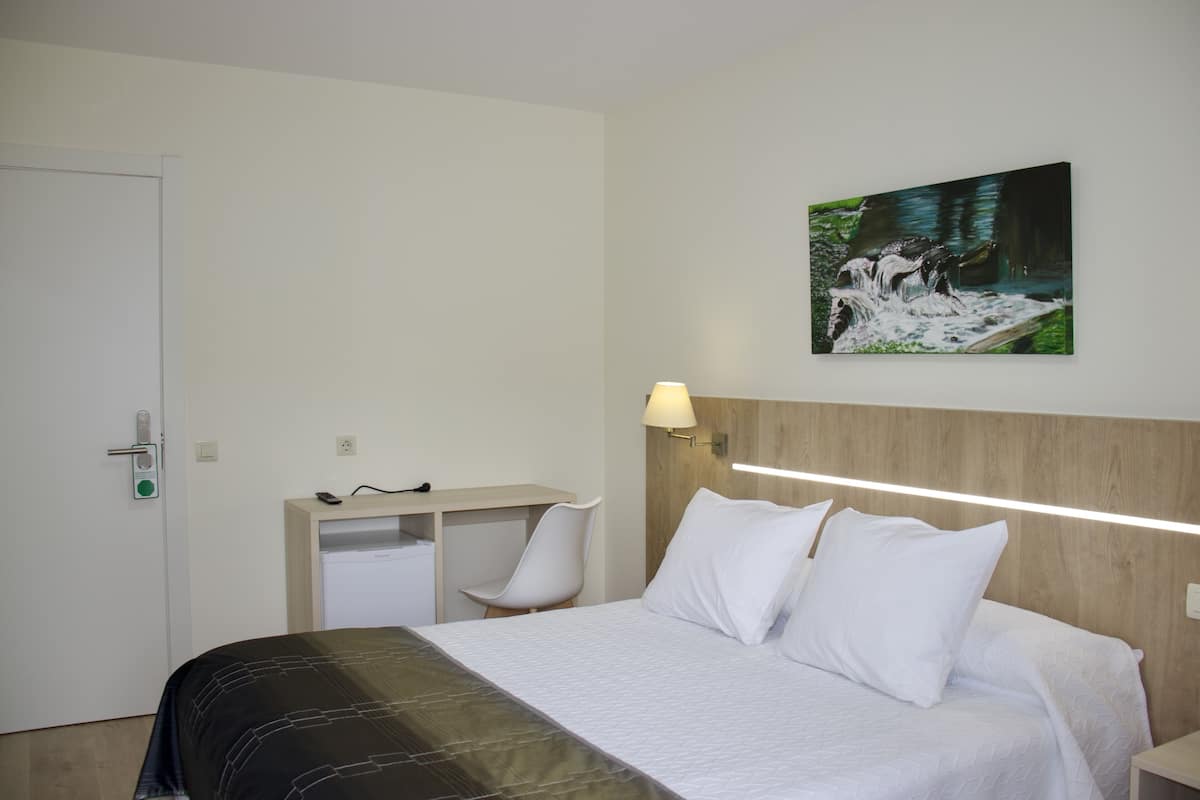 Habitación de hotel con cama, escritorio, silla, lámpara de pared y un cuadro.