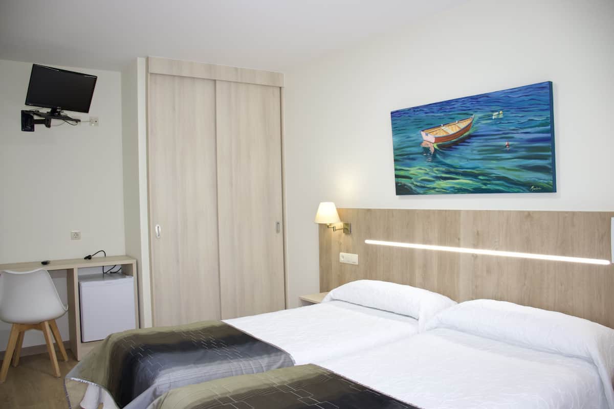 Habitación de hotel con una cama, un escritorio con una computadora, un televisor montado en la pared y un cuadro de un barco.