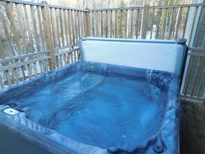 Un jacuzzi con panel de control, rodeado por una terraza de madera y un cerco de madera.