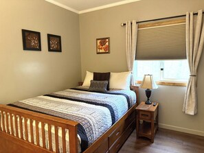 Un dormitorio con una cama de madera, una mesita de noche, una lámpara y un ventanal con cortinas.