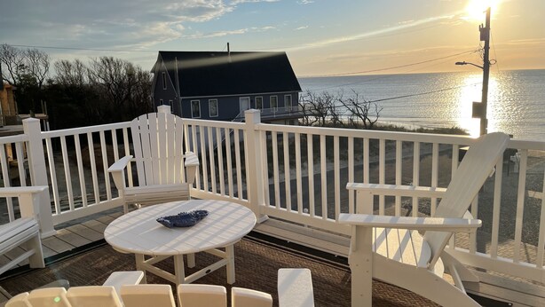 Une terrasse avec des chaises blanches et une table, d’où l’on a vue sur une étendue d’eau et une maison.