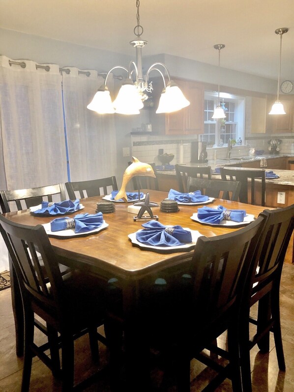 A dining area with a round wooden table set for six, surrounded by dark chairs. A decorative dolphin sculpture is placed on the table.