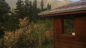 A wooden cabin with a single window and a deck with a chair and cushions.