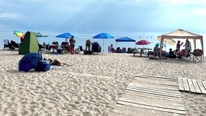 Ein Strand mit mehreren Sonnenschirmen, einem Zelt und entspannten Personen.