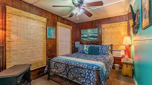 Une chambre à coucher avec un lit, un ventilateur de plafond, un radiateur et des murs en bois.