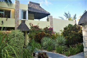 Un bâtiment moderne doté d’une façade en pierre, d’un toit de chaume et d’une grande variété de plantes tropicales.