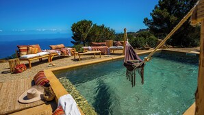 Un espace aménagé au bord de la piscine, avec des chaises longues et un hamac, offrant une vue sur une mer d’un bleu limpide.