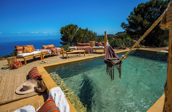 A poolside area with lounge chairs and a hammock, overlooking a clear blue sea.
