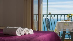 Une chambre d’hôtel avec un lit, un balcon doté d’une table et de chaises, et une vue sur la mer.