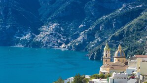 Une ville côtière aux bâtiments à étages, une église imposante surmontée d’un dôme doré et une vue dégagée sur la mer.