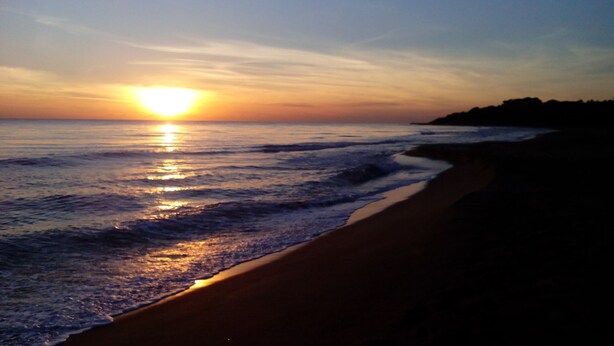 Uma praia ao pôr do sol, com o sol refletindo na água.