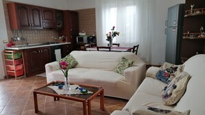 Uma sala de estar com sofá, mesa de centro e área de cozinha com armários e micro-ondas.