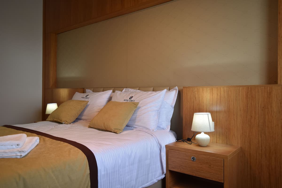 A hotel room with a bed, pillows, a nightstand, and a lamp.