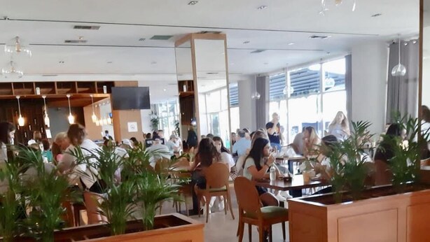 A modern restaurant with wooden furniture, large windows, and hanging light fixtures.