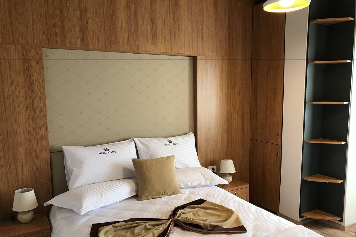 A neatly made bed with white linens and two pillows, a bedside table with a lamp, and a wooden headboard.