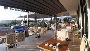 An outdoor café with tables and chairs, a covered area, and a view of the surrounding landscape.