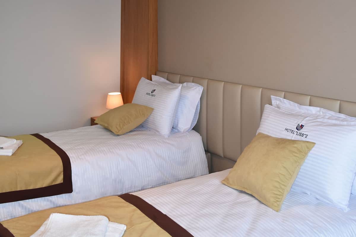 A hotel room with two beds, each with white bedding and a brown headboard. There is a hanging light fixture above the beds.