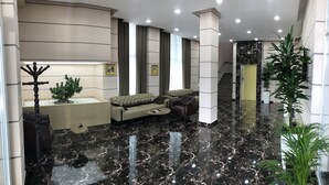 A modern lobby with a black marble floor, a beige sofa, a leather armchair, and a potted plant.