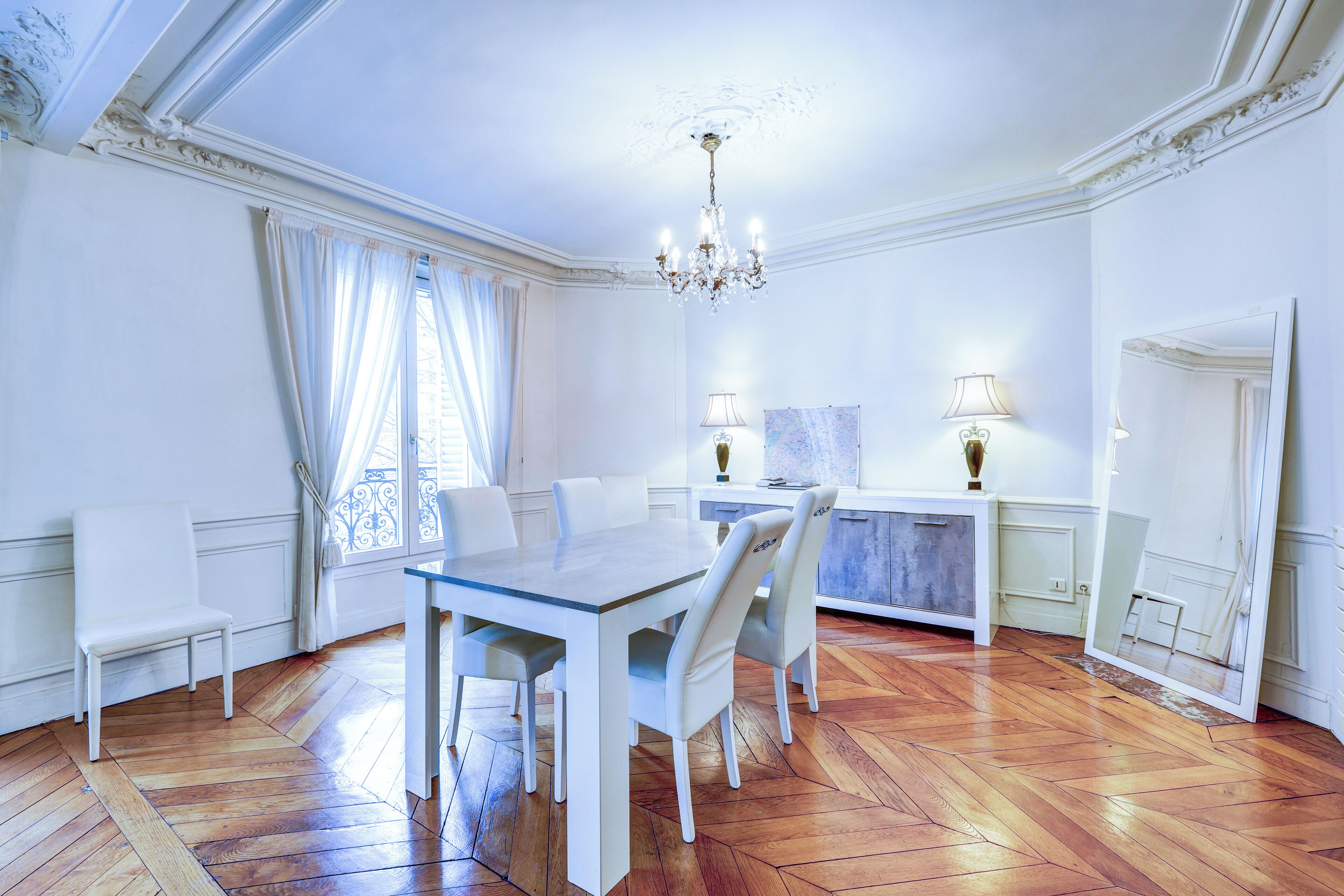 Un espace repas comprenant une table et des chaises, un lustre et une vue sur l’extérieur par une fenêtre agrémentée de rideaux.