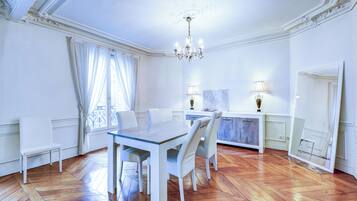 Un espace repas comprenant une table et des chaises, un lustre et une vue sur l’extérieur par une fenêtre agrémentée de rideaux.