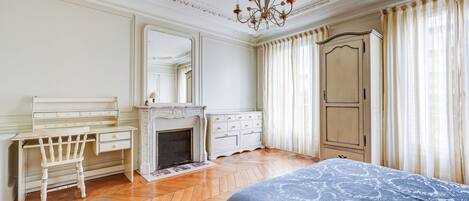 A bedroom with a bed, a desk, a chair, a wardrobe, and a fireplace.