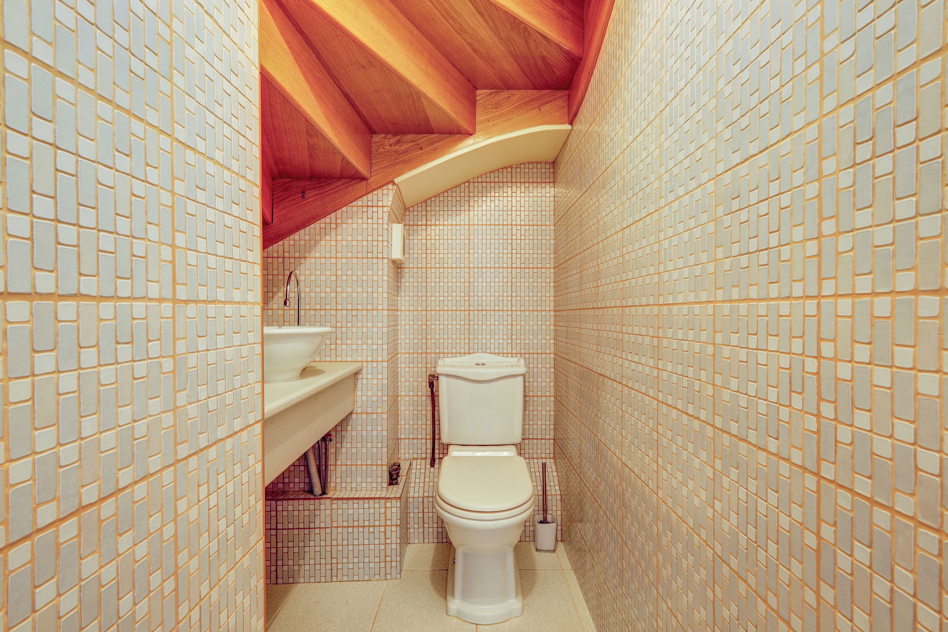 A bathroom with a tiled floor, a toilet, a sink, and a wooden ceiling.