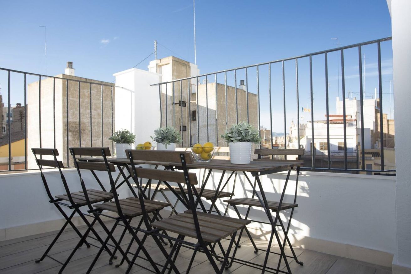 A balcony with a table and chairs, potted plants, and a view of buildings.