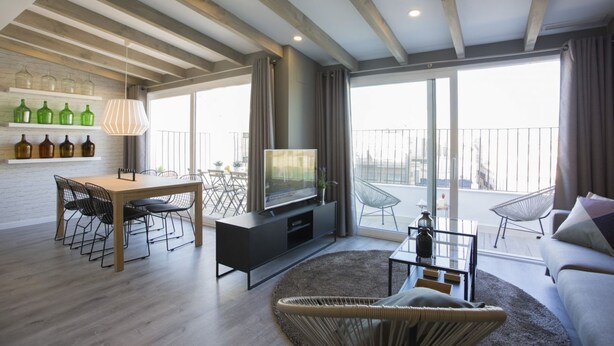 Een moderne woonkamer met een houten plafond, een eethoek met tafel en stoelen, een flatscreen-tv en een balkon met uitzicht.