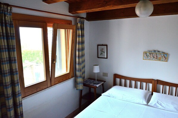 Un dormitorio con una cama de madera, una mesita de noche con una lámpara y una ventana con cortinas.