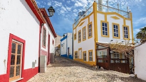 A cobblestone street lined with colorful buildings, a wooden fence, and a clear blue sky. - Alto Club, Alvor. Quiet, comfortable apartment in this acclaimed holiday resort (Alvor)