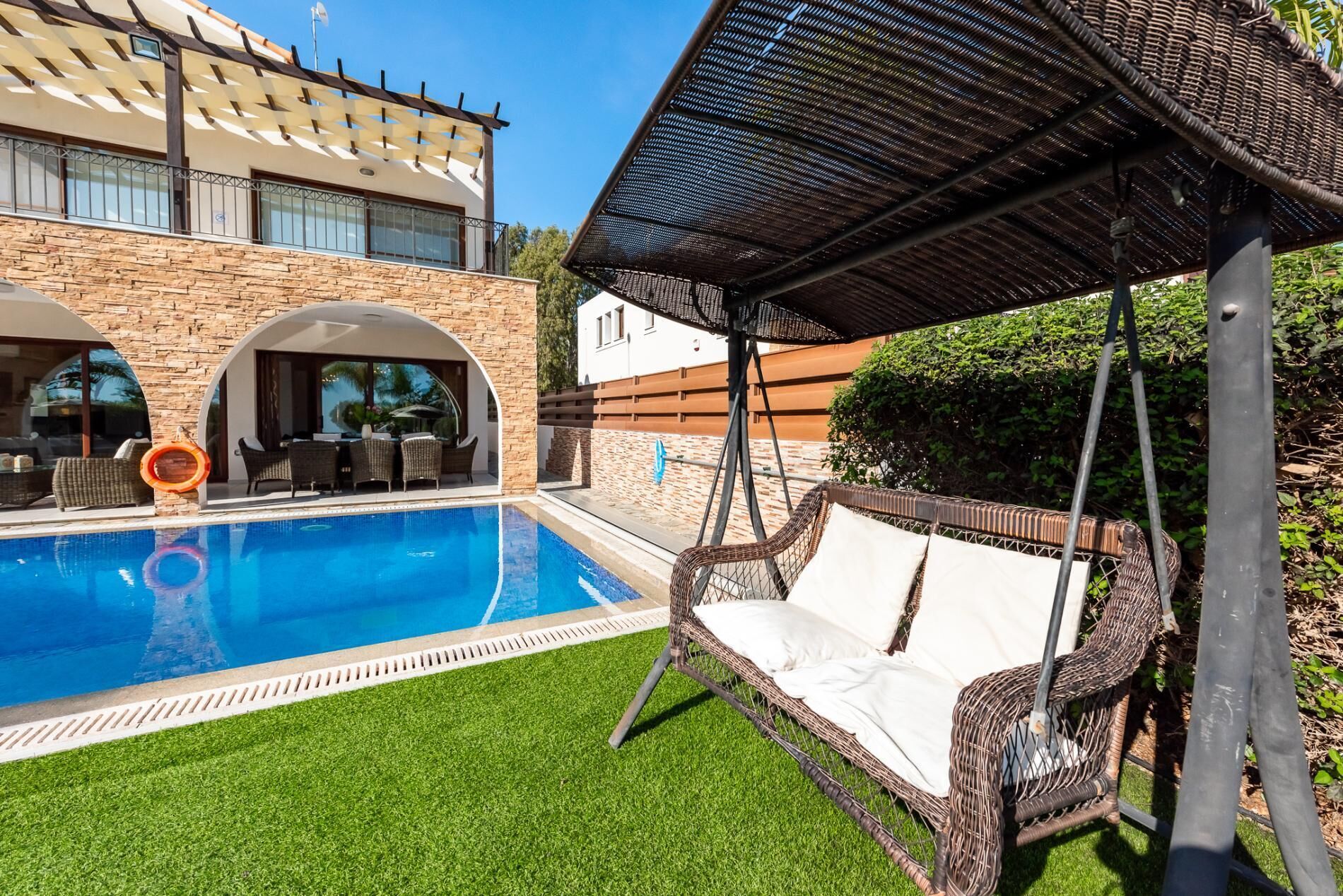 Una piscina con una silla colgante de mimbre y una zona de estar techada.