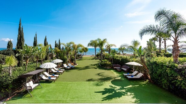 A pool area with sun loungers, umbrellas, and a view of the ocean.