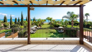 A balcony with a view of a well-maintained garden and the sea.