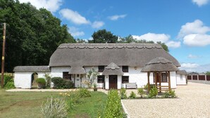 A traditional thatched-roof house with a white exterior, a small porch, and a gravel driveway. - Luxury villa for 22 people with pool, jacuzzi, large garden and private pub! (Three Legged Cross)