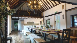 A dining area with a long table set for a meal, wooden benches, and a chandelier. - Luxury villa for 22 people with pool, jacuzzi, large garden and private pub! (Three Legged Cross)