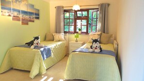 Ein Zimmer mit zwei Betten, jeweils mit einem kuscheligen Hundespielzeug, einem Nachttisch mit Lampe und einem Fenster mit Vorhängen.
