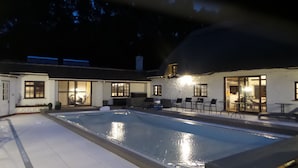 A swimming pool with a patio area, outdoor seating, and a building with large windows and doors. - Luxury villa for 22 people with pool, jacuzzi, large garden and private pub! (Three Legged Cross)