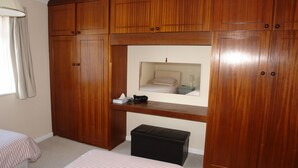 Ein Schlafzimmer mit einem Holzschrank, einem Bett, einer kleinen Bank und einem Fenster mit Vorhängen.