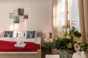 Una cama bien hecha con una manta roja, una mesita de noche con lámpara y una pared con cuadros.