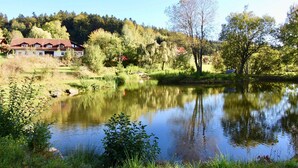 A house with a red roof near a calm lake surrounded by trees.